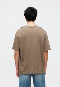 Braunes kurzärmeliges T-Shirt aus weicher Baumwolle mit lockerem Schnitt und Rundhalsausschnitt, kombiniert mit hellblauen Jeans.