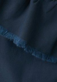 Tissu bleu foncé avec une texture douce et un bord à franges, plié pour montrer les couches et les détails subtils du tissage.