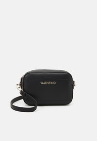 Bolso cruzado de cuero negro con un logo dorado, forma rectangular, cierre con cremallera y correa ajustable. Acabado texturizado sutil.