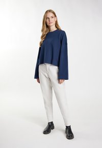 Granatowy krótki sweatshirt z długimi rękawami, połączony z białymi spodniami i czarnymi botkami na kostkę, stojący na neutralnym tle.