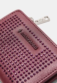 Rosa faux læderpung med en nitterdesignet, skinnende lilla accenter og en sølvlynlås med en mærket trækstang.