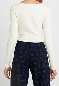 Kerman ribbetttu pitkähihainen paita, jossa on syvään laskettu kaula-aukko, yhdistettynä laivastonsiniset ruudullisiin korkeavyötäröisiin housuihin, jotka ovat rentoa mittaa ja joissa on taskut.