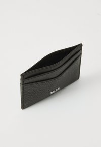 Crni kožni držač za kartice s teksturiranom površinom, s utorima za kartice i elegantnim, minimalističkim dizajnom. Nema vidljivih metalnih dijelova ili ukrašavanja.