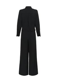 Fekete overál hosszú ujjakkal, övvel a deréknál és széles lábakkal. Galléros nyakkal és hátsó varrás részlettel rendelkezik. Simább anyagtextúra.