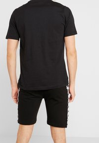 Černé bavlněné tričko s klasickým kulatým výstřihem, spárované s černými šortkami s bílými postranními pruhy. Jednoduchý, pohodlný design.