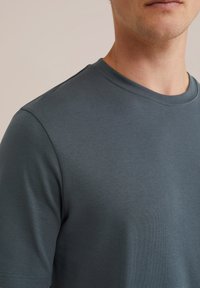 Camiseta de algodón gris oscuro con escote redondo, mangas cortas y textura suave, con un diseño minimalista sin adornos.