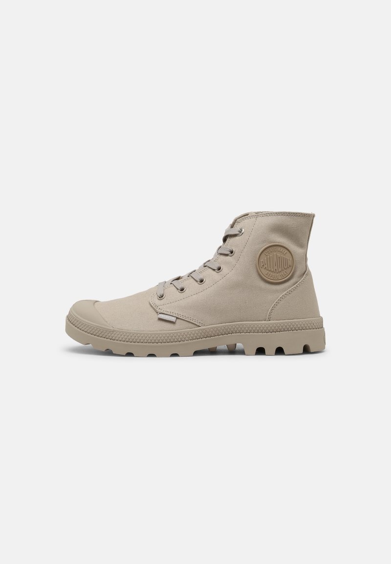 Bottine beige en toile à lacets avec semelle en caoutchouc et bout arrondi, ornée d'un patch rond avec le logo Palladium à la cheville.