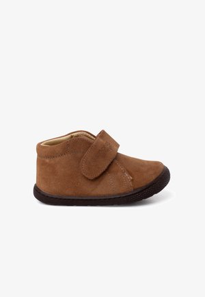 Zapato infantil de ante marrón con una correa de velcro, puntera redonda, forro interior suave y suela de goma negra texturizada.