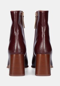 Botas de tobillo de cuero burdeos con textura suave, cremalleras laterales y tacones gruesos a rayas marrones. Vista trasera que muestra la altura del tacón.