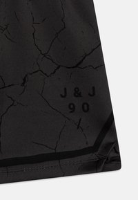 Nærbillede af et sort stof med et revnet mønster, en sort kantlinje og sort tekst der læser "J & J 90" nær kanten.