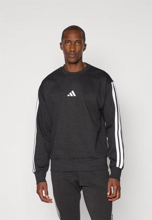 Crna dukserica napravljena od mješavine pamuka s bijelim Adidas logotipom, rebrastim manžetama i tri bijele trake duž rukava.