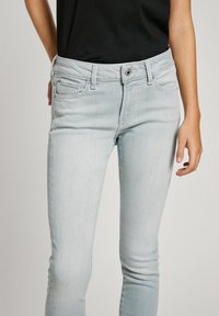 Vaqueros ajustados de color azul claro con una textura suave, cinco bolsillos y cierre de cremallera. Presentan un ligero estiramiento para mayor comodidad.