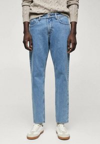 Vaqueros azul claro con un ajuste relajado, piernas rectas y diseño de cinco bolsillos, combinados con zapatillas blancas y beige y un suéter de punto.