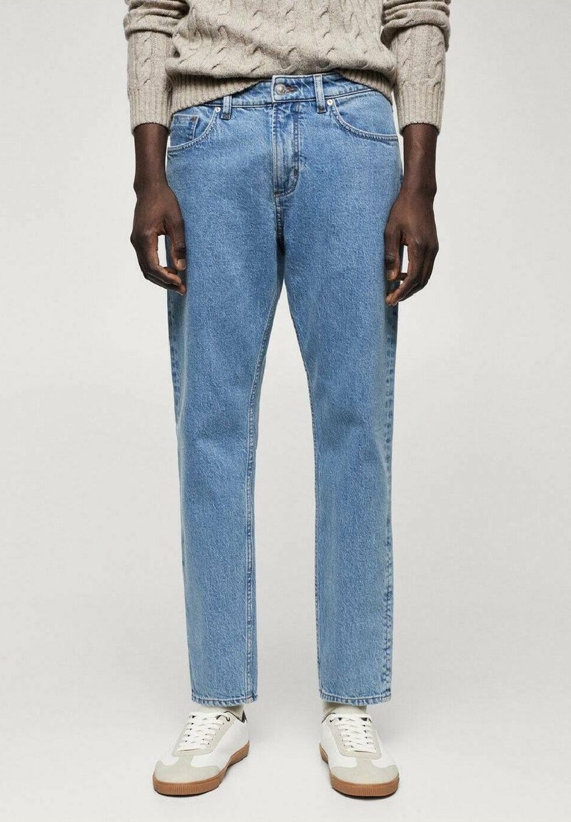 Vaqueros azul claro con un ajuste relajado, piernas rectas y diseño de cinco bolsillos, combinados con zapatillas blancas y beige y un suéter de punto.