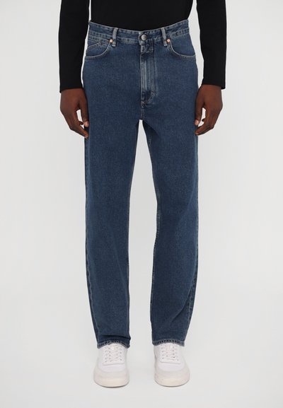 Dunkelblaue Denim-Jeans mit entspannter Passform, mit Five-Pocket-Styling und einem klassischen Knopf- und Reißverschluss. Getragen mit weißen Turnschuhen.