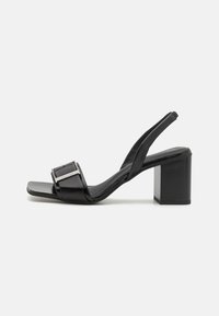 Black slingback heels with a square toe, block heel, and metallic buckle detail. Made of smooth synthetic material.