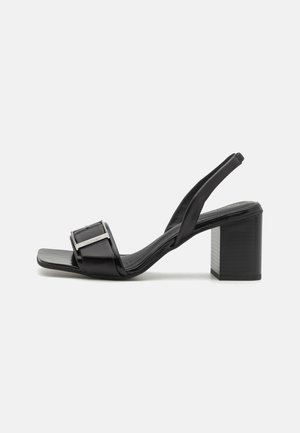 Black slingback heels with a square toe, block heel, and metallic buckle detail. Made of smooth synthetic material.