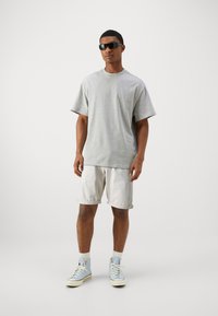 Camiseta gris de manga corta combinada con pantalones cortos ligeros enrollados. Usada con zapatillas altas azules y gafas de sol negras. Fondo neutro.