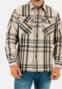 Rutig flanellskjorta i beige, brun och blå. Har två bröstfickor med lock, knappstängning och krage. Mjuk textur.