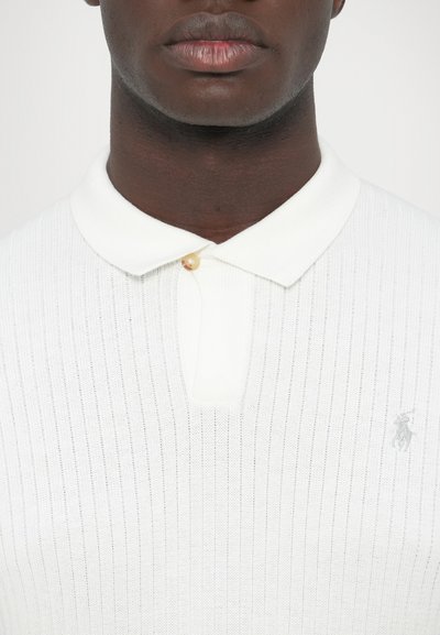 Biela rebrovaná polokošeľa s jemnou textúrou, so zapínaním na dva gombíky a malým sivým logom na hrudi.