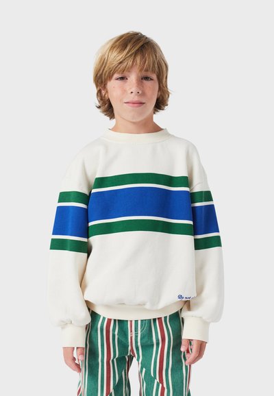 Felpa bianca con righe orizzontali blu e verdi, polsini e orlo a coste, abbinata a pantaloni a righe verticali verdi e rossi.