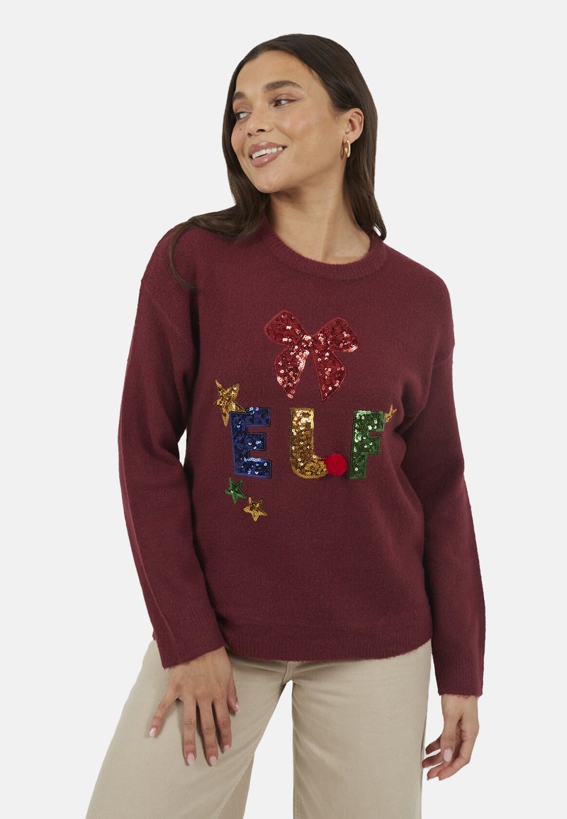 Pull marron avec le texte "ELF" coloré en sequins, un nœud rouge et des accents d'étoiles. Texture douce avec une coupe décontractée et un col côtelé.