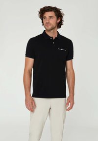 Camisa polo negra fabricada en una mezcla de algodón, con cuello, tapeta de tres botones y acentos blancos en las mangas. Logo en el pecho.
