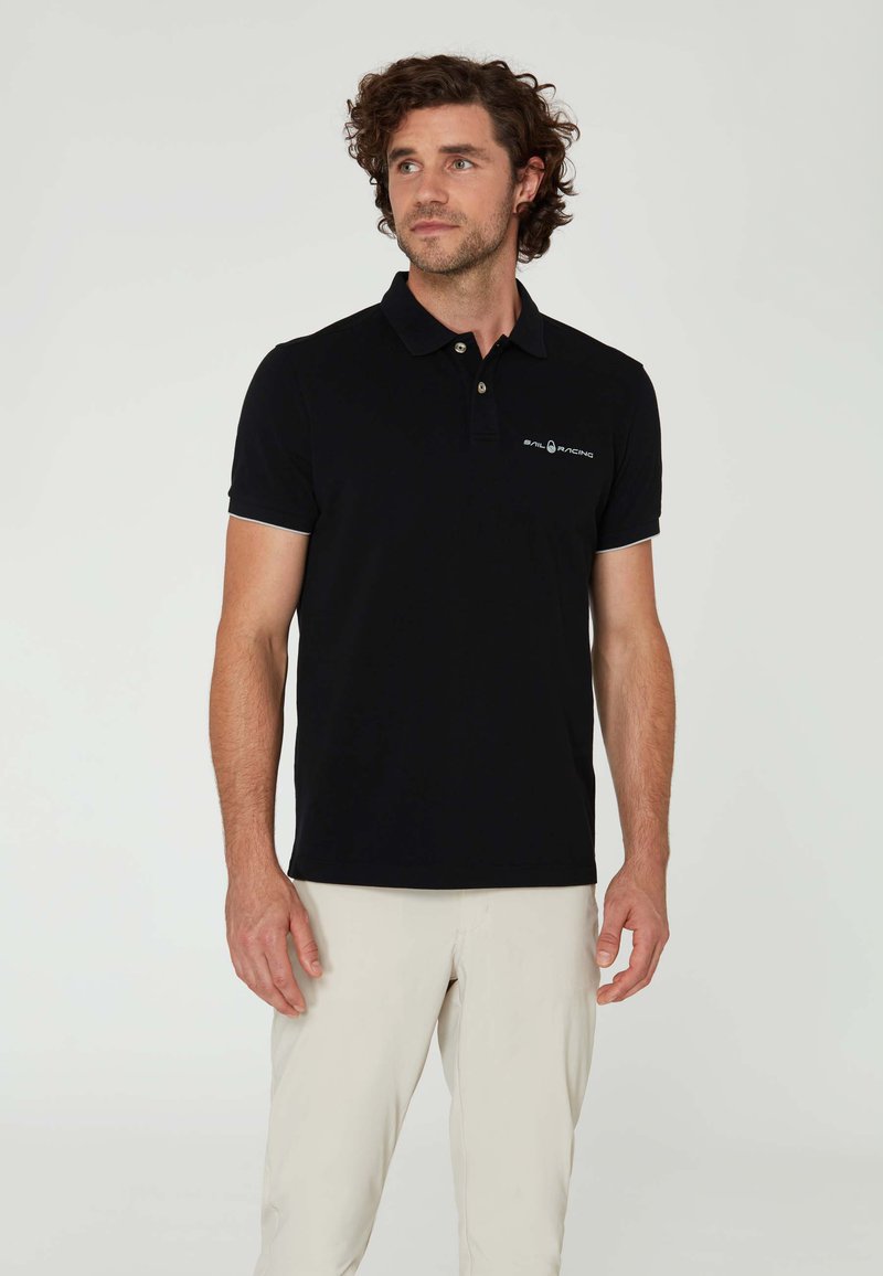 Camisa polo negra fabricada en una mezcla de algodón, con cuello, tapeta de tres botones y acentos blancos en las mangas. Logo en el pecho.