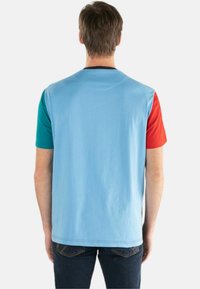T-shirt med korte ærmer i farveblokering med en lys blå ryg og teal og rød aksenter på ærmerne; lavet af blødt stof med en glat tekstur.