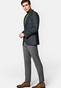 Zielona marynarka w kratę z niebieskimi akcentami, zestawiona z szarym golfem, szarymi spodniami i brązowymi butami, podkreślająca dopasowany fason i czyste linie.