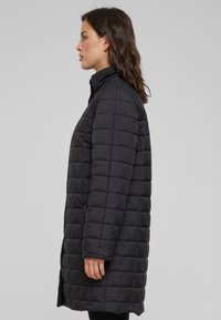 Čierna prešívaná puffer bunda s vysokým golierom, dlhými rukávmi a rovnými líniami, ktorá sa vyznačuje hladkým povrchom a mriežkovým vzorom.