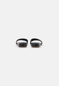 Sandalias negras con material superior suave, que cuentan con dos correas delgadas y una suela plana. Diseño funcional con acentos minimalistas.