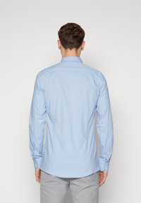 Chemise à manches longues bleu clair avec col boutonné, faite d'un tissu lisse, présentant un dos droit et des poignets à boutons.