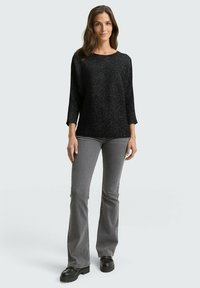 Haut noir texturé à manches trois-quarts, associé à un jean gris évasé. Des chaussures à plateforme noires complètent la tenue. Design simple et moderne.