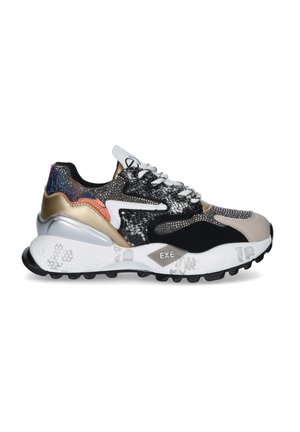 Zapatilla deportiva de corte bajo con materiales mixtos en negro, beige, dorado y plateado, cordones blancos, suela texturizada y estampados decorativos en la entresuela.