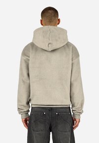 Pelēka fleecveida kapuce ar kapuci, ribveida aprocēm un vienkāršu dizainu. Iekšpuse izskatās mīksta, ar brīvu piegriezumu un bez redzama zīmola.