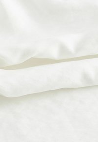 Biała bawełniana tkanina o miękkiej teksturze z lekko pomarszczonymi warstwami. Materiał wydaje się gładki i lekki.