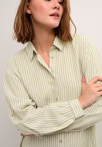 Chemise boutonnée à rayures vert clair et blanches avec manches longues. Présente un col classique et des poignets froncés pour plus de texture.