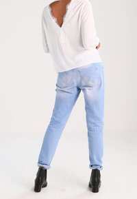 Blusa bianca con pizzo sul retro, abbinata a jeans azzurri con risvolto e stivali neri con tacco. Look pulito e casual.