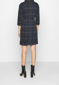 Marinblå rutig klänning med trekvartslånga ärmar, krage och en figursydd silhuett, i kombination med svarta ankelboots och klossklack.