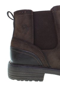 Hnědá kožená kotníková bota s elastickými postranními panely, texturovaným povrchem a gumovou podrážkou. Obsahuje dekorativní švy a logo.