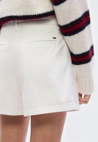 Λευκό βαμβακερό σορτς με ευθεία γραμμή, που διαθέτει πίσω τσέπη, συνδυασμένο με κρεμ πουλόβερ με κόκκινες και ναυτικές οριζόντιες ρίγες.