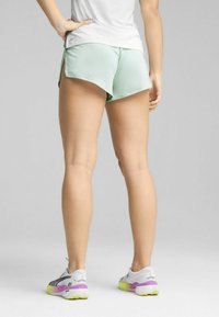 Shorts de sport vert menthe avec une coupe ample et des fentes latérales, associés à des baskets grises et blanches avec une semelle jaune et violette.