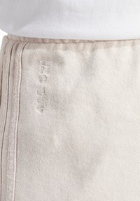 Pantaloni della tuta color beige chiaro con una consistenza morbida, caratterizzati da un sottile ricamo laterale e cuciture a contrasto.
