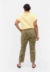 Žluté tričko s krátkým rukávem zkombinované s kalhotami se vzorem maskáče, se rovnými nohavicemi a kapsami, viděné zezadu.