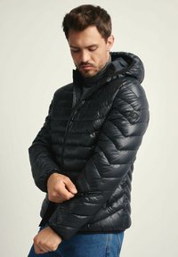 Puchowa czarna kurtka z kapturem, z zamykaną na zamek kieszenią na nadgarstku i pikowanym wzorem. Wykonana z błyszczącego, lekkiego materiału.