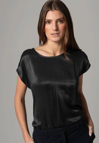 Schwarze Satinbluse mit lockerer Passform, Rundhalsausschnitt und kurzen Ärmeln. Glatte Textur, die sanft über den Körper fällt.