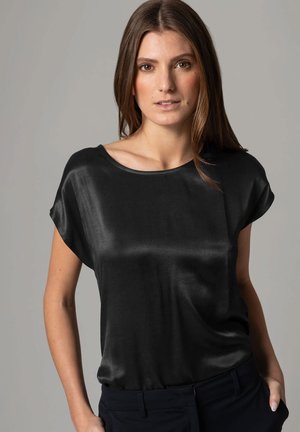 Zwarte satijnen blouse met een losse pasvorm, ronde halslijn en korte mouwen. Gladde textuur die zacht over het lichaam valt.