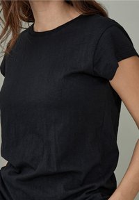Černé tričko s krátkým rukávem z texturované látky, s kulatým výstřihem a volnějším střihem. Bez viditelných vzorů nebo ozdob.