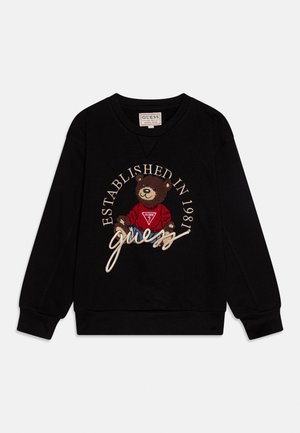 Felpa nera a maniche lunghe con un orsetto che indossa un maglione rosso Guess, con le scritte "Established in 1981" e "Guess" ricamate.